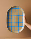 Robert Gordon Coastal Junction 38cm oval stoneware tray with blue handbrush grid design held against beige background