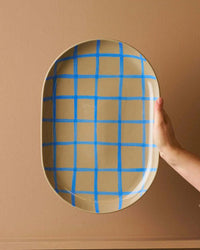 Robert Gordon Coastal Junction 38cm oval stoneware tray with blue handbrush grid design held against beige background