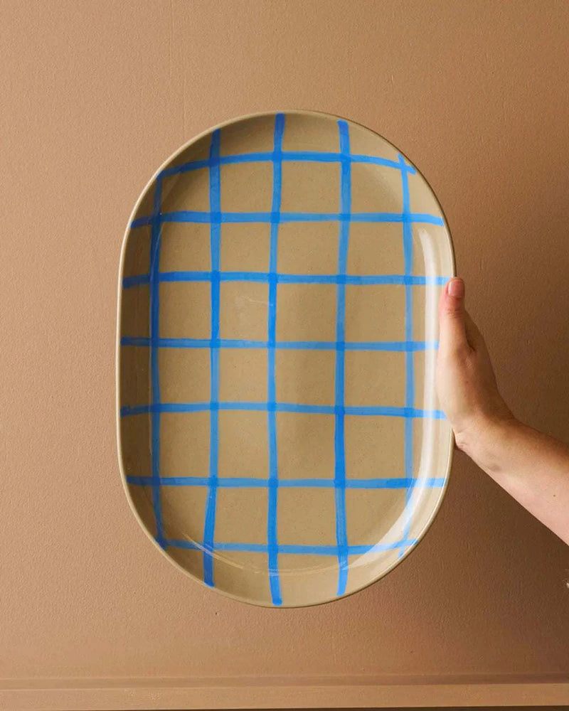 Robert Gordon Coastal Junction 38cm oval stoneware tray with blue handbrush grid design held against beige background