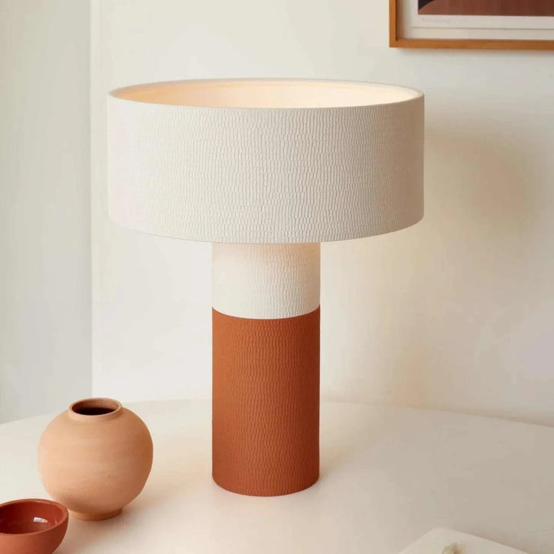 POTT Lighting Terra Table Lamp in matte white and dark terracotta with textured ceramic base and white cylindrical shade on a neutral surface