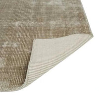 GlobeWest Tepih Tide Rug Oyster color hand woven viscose and wool with ocean ripple design, indoor area rug with soft texture and folded corner showing underside.