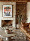 Marcia Priestley Limited Edition fine art canvas print titled Rachero, framed in a floating oak frame, displayed in a rustic living room with leather sofa and cactus plant.