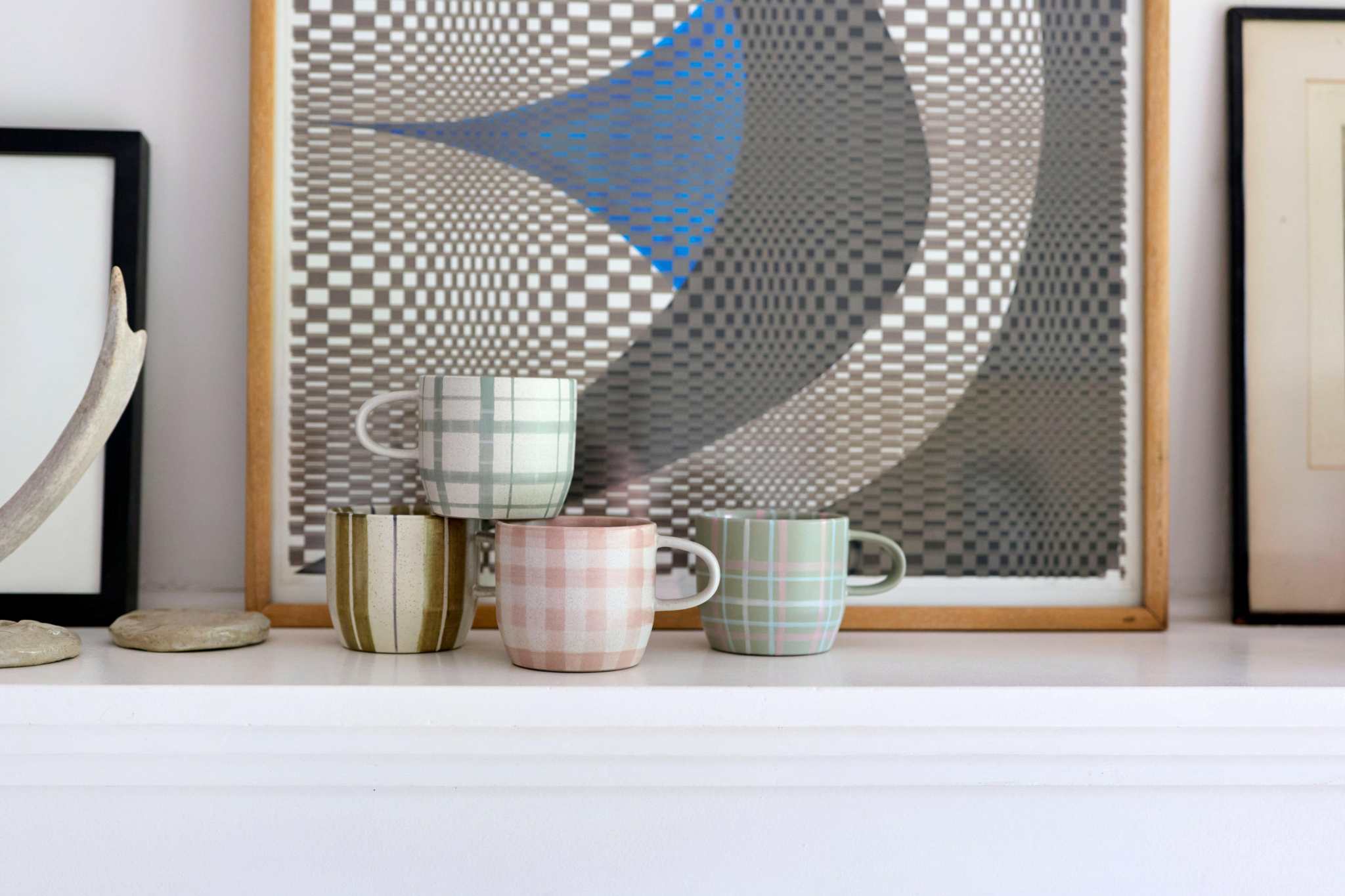 Set of four Robert Gordon hand-painted mugs with plaid, striped, and gingham designs displayed on a white shelf.