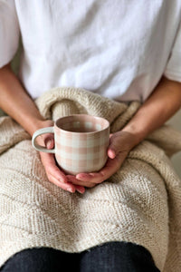 Robert Gordon hand-painted soft terracotta check ceramic mug held by person wrapped in knitted blanket