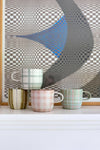 Set of four Robert Gordon mugs with hand-painted tartan, stripes, and gingham checks in muted colors on a white surface.