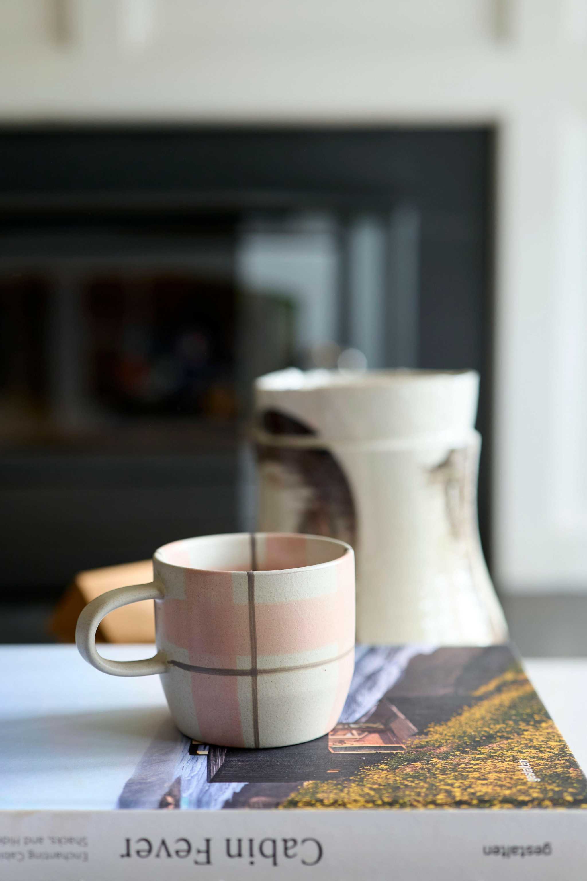 Robert Gordon Hand-Painted Mug in blush and grey tartan ceramic design placed on a book