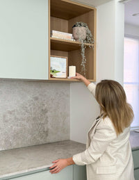 Woman styling wooden kitchen shelves with books and decorative items in modern home interior