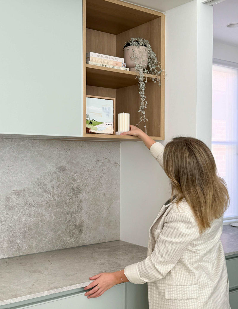 Woman styling wooden kitchen shelves with books and decorative items in modern home interior