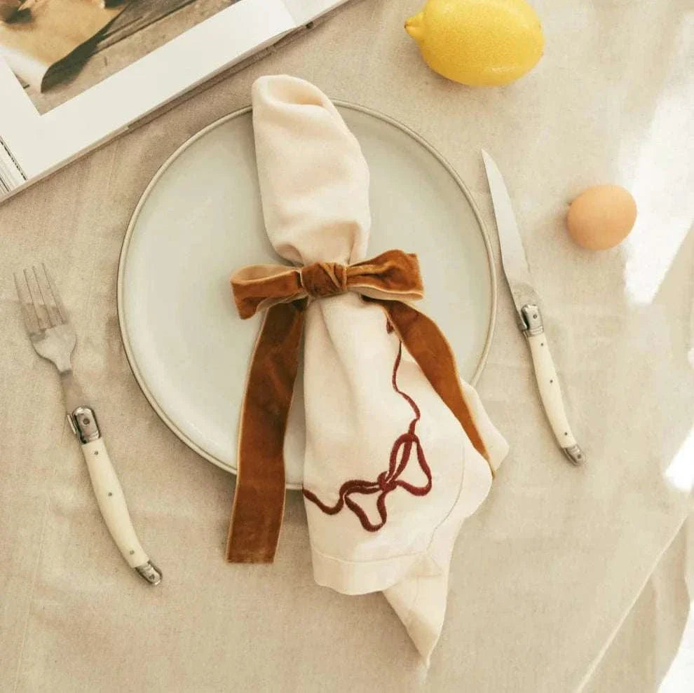 Same Time Tomorrow Napkin Ring in caramel velvet bow on white napkin placed on plate with cutlery and lemon nearby