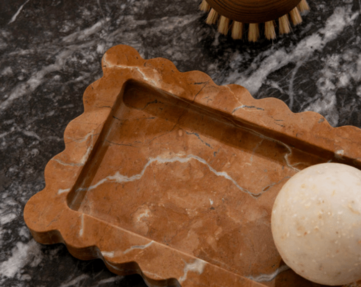 CoTheory Palazzo Scalloped Marble Tray in Rosso Alicante with scalloped edges and narrow profile on dark marble surface