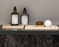 Beige travertine Palazzo Scalloped Marble Bar Tray with soap, brush, and lotion bottles on black shelf