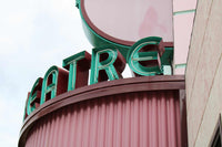 Vintage theatre sign with green neon letters on a maroon corrugated facade against a cloudy sky, theatre print wall art.