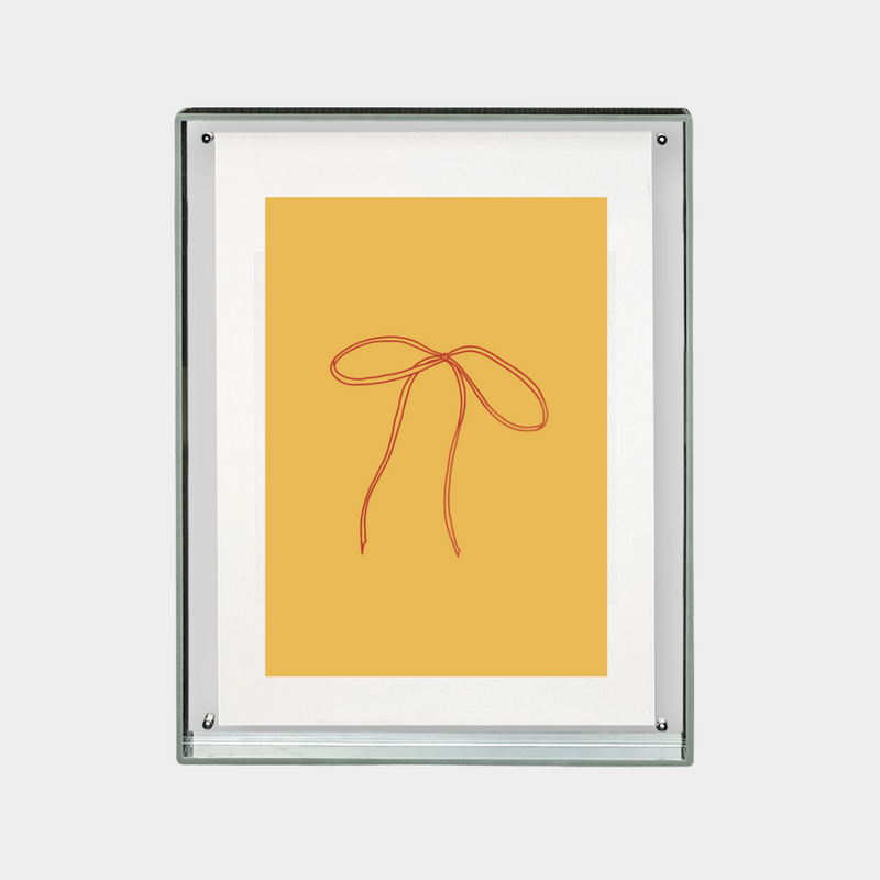 minimalist digital print of red ribbon bow on mustard yellow background in a clear frame