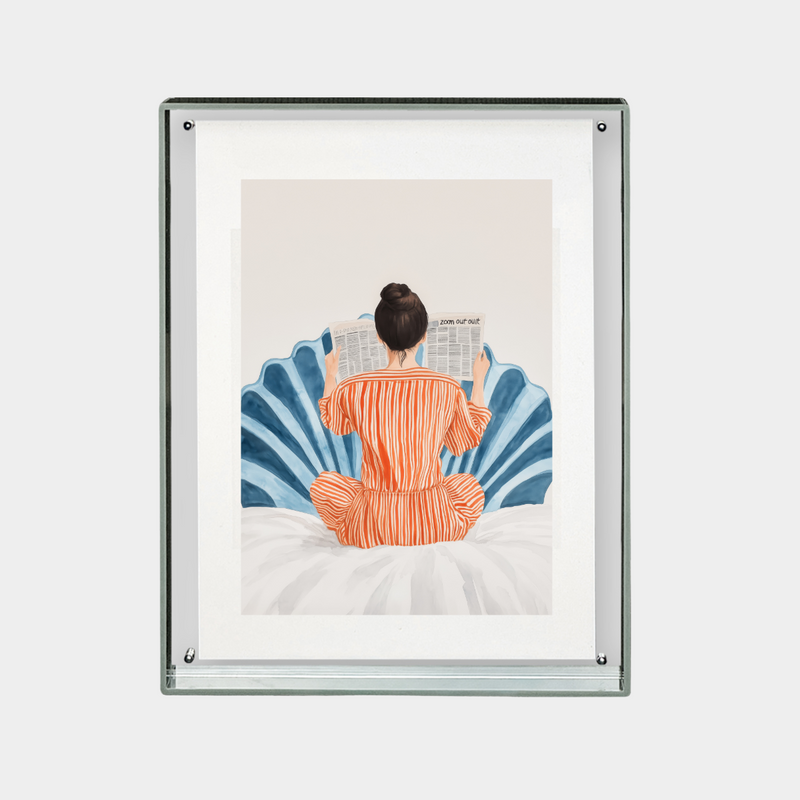 Framed digital print of person in orange pajamas reading newspaper on bed against blue decorative background