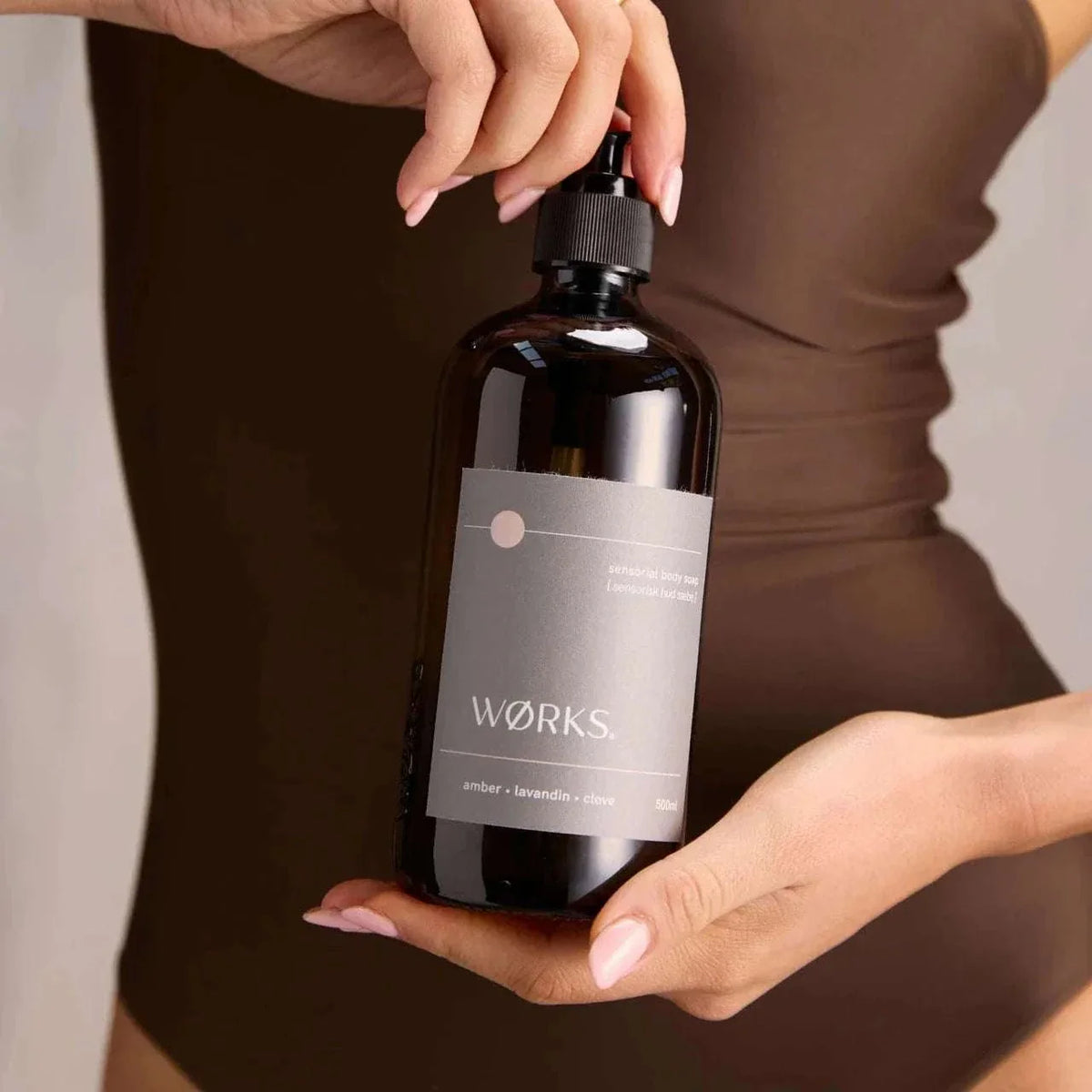 Hand holding amber Works Body Soap in 500ml dark glass bottle with pump dispenser.