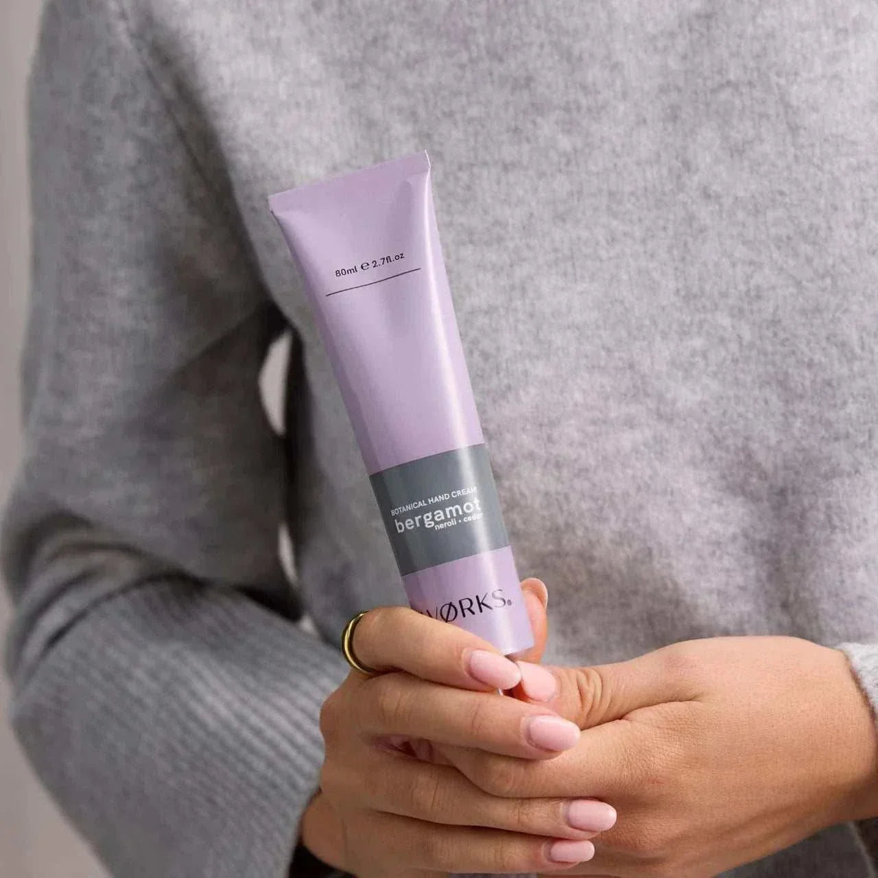Person holding a lavender tube of plastic-free natural hand cream with soft pink nails, promoting Selfie Nails Express Gel Polish - BLUSH.