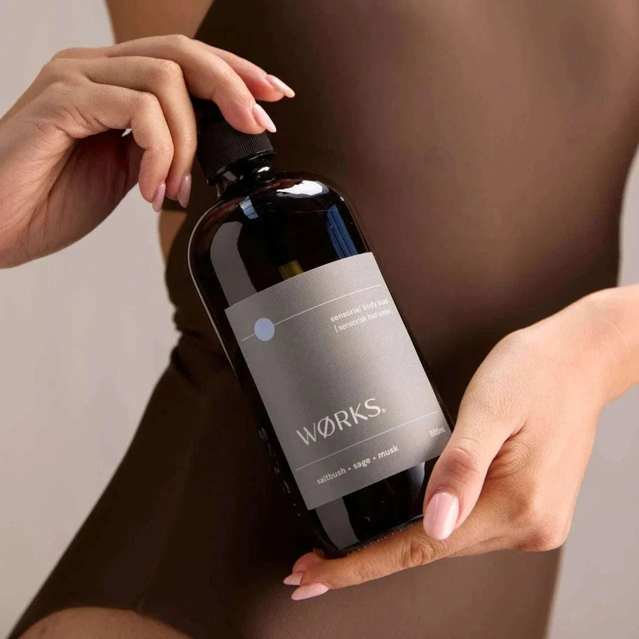 Hand holding Works Body Soap Salt Bush 500ml in a smoky grey glass bottle with minimalist label design