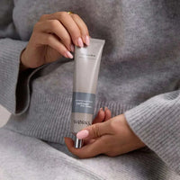 Person holding a tube of Works Hand Cream Vetiver 80ml with a gray outfit background