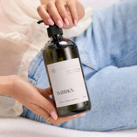Hand holding 500ml bottle of Works Hand Soap with vetiver scent in smoky grey glass packaging