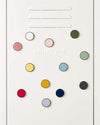 Mustard Made magnetic buttons in various colors arranged on a white surface with embossed logo