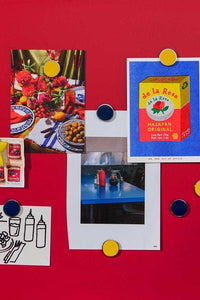 Mustard Made navy blue magnetic buttons holding photos and postcards on a red magnetic board
