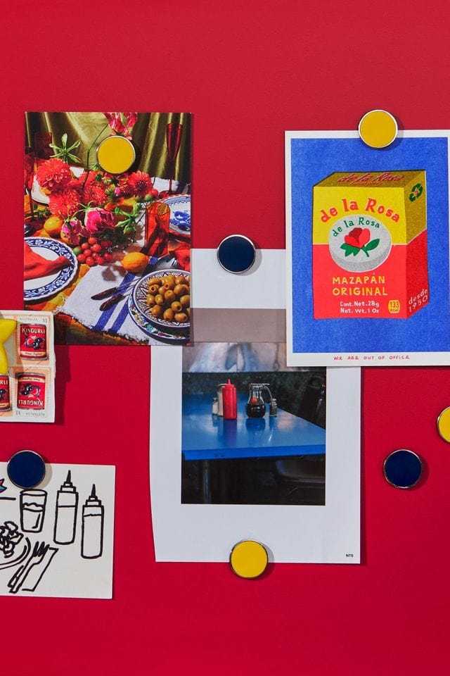 Mustard Made navy blue magnetic buttons holding photos and postcards on a red magnetic board