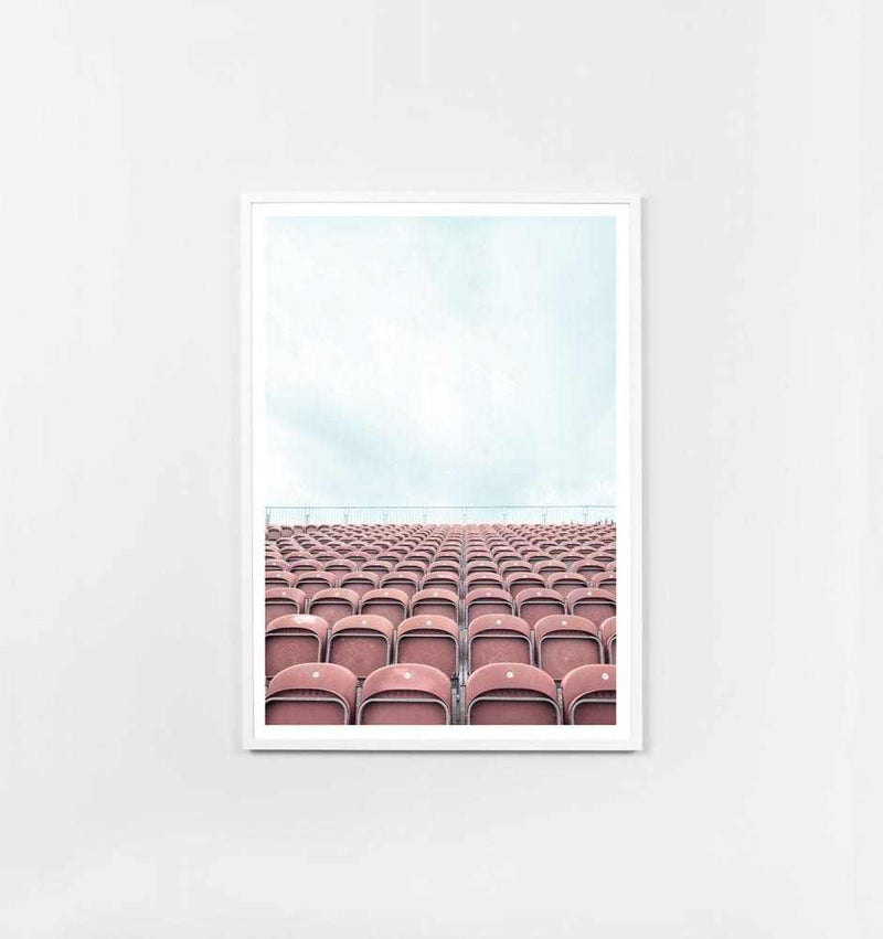 Framed photographic print titled "Middle of Nowhere Arena Dusty Pink" showing rows of dusty pink seats under a light blue sky with a white border and oak frame.