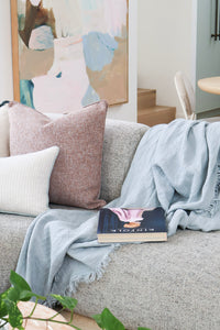 Aura cushion layered with neutral cushions and a blue linen throw