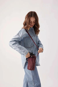 Woman wearing burgundy Base Supply Bottle Sling crossbody bag with adjustable strap and soft crinkle fabric carrying a water bottle