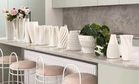 Row of white matte ceramic Bailey decorative vases with varied curved and textured designs displayed on a kitchen countertop