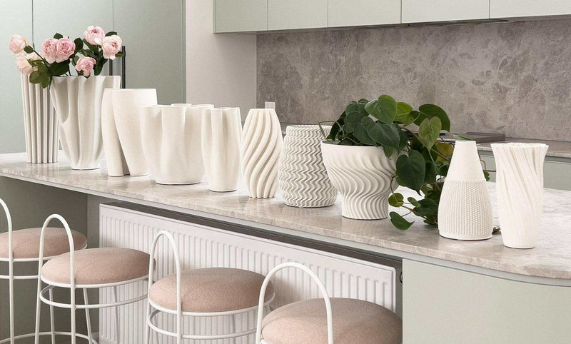Row of white matte ceramic Bailey decorative vases with varied curved and textured designs displayed on a kitchen countertop