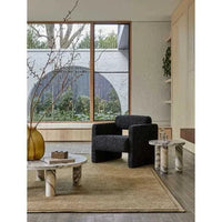 GlobeWest Bower Frame Rug in moss color, hand-woven wool, placed in modern living room with marble tables and large window.