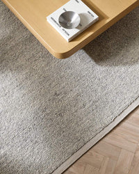 Baya Clifton Floor Rug in ash color with hand-knotted wool loop pile texture under wooden table corner