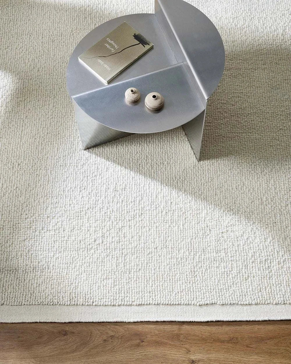 Baya Clifton Floor Rug ivory hand-knotted wool loop pile with flat edge on wooden floor with round modern metal table