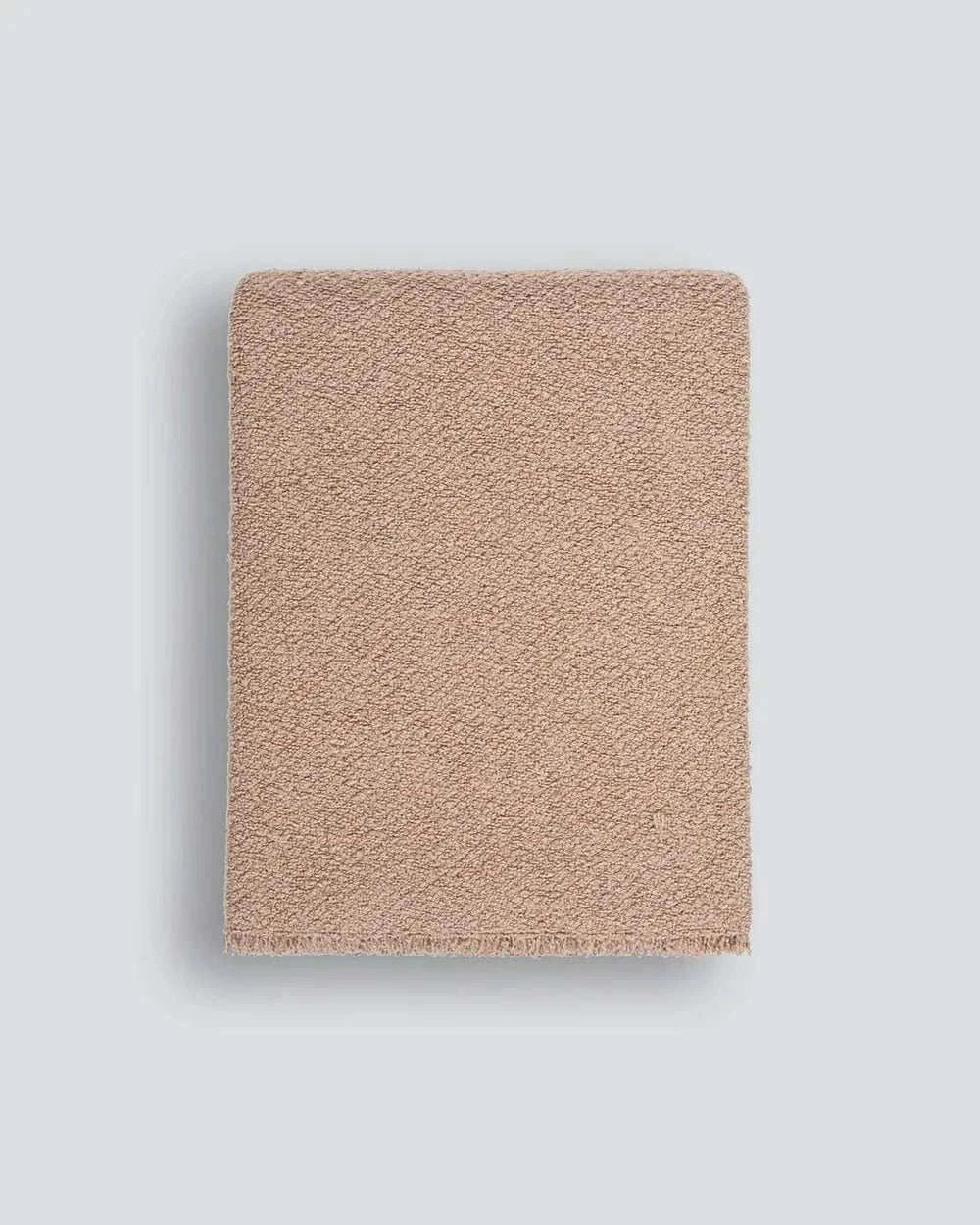 Blush Baya Cromwell Throw Blanket with textured cotton blend bouclé weave and short raw-edge fringing draped over sofa