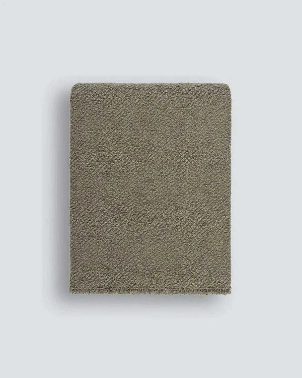 Baya Cromwell Throw Blanket in dusky olive green cotton blend bouclé texture draped on sofa