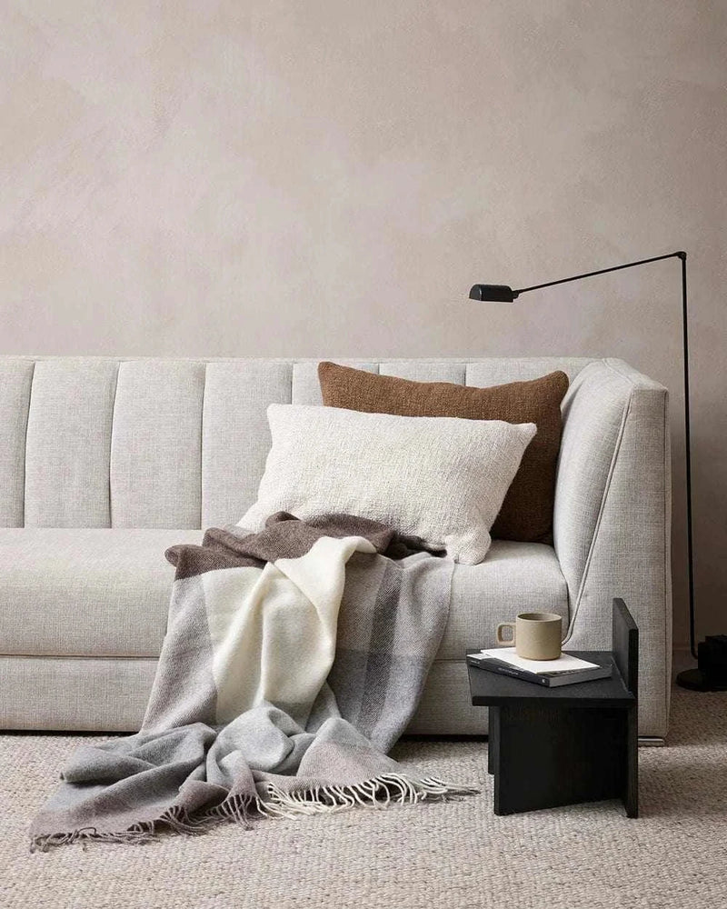 Baya Cyprian Oblong Cushion in oatmeal on a light sofa with cozy throw and side table.
