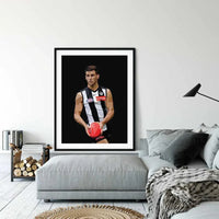 Framed Dom Gauci Kids Art Print of AFL player Nick Daicos in Collingwood FC jersey displayed above grey couch in modern living room