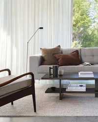 Living room with grey sofa featuring Baya Dover Cushion in brick color and brown cushions, modern wooden armchair, and coffee table with books and decor