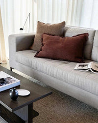 Baya Dover Cushion in brick color with fringed edges on a grey sofa in a modern living room