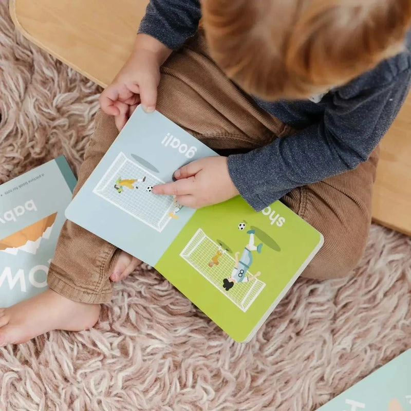 Child reading a colorful soccer-themed board book from the Soccer Baby series on a soft rug