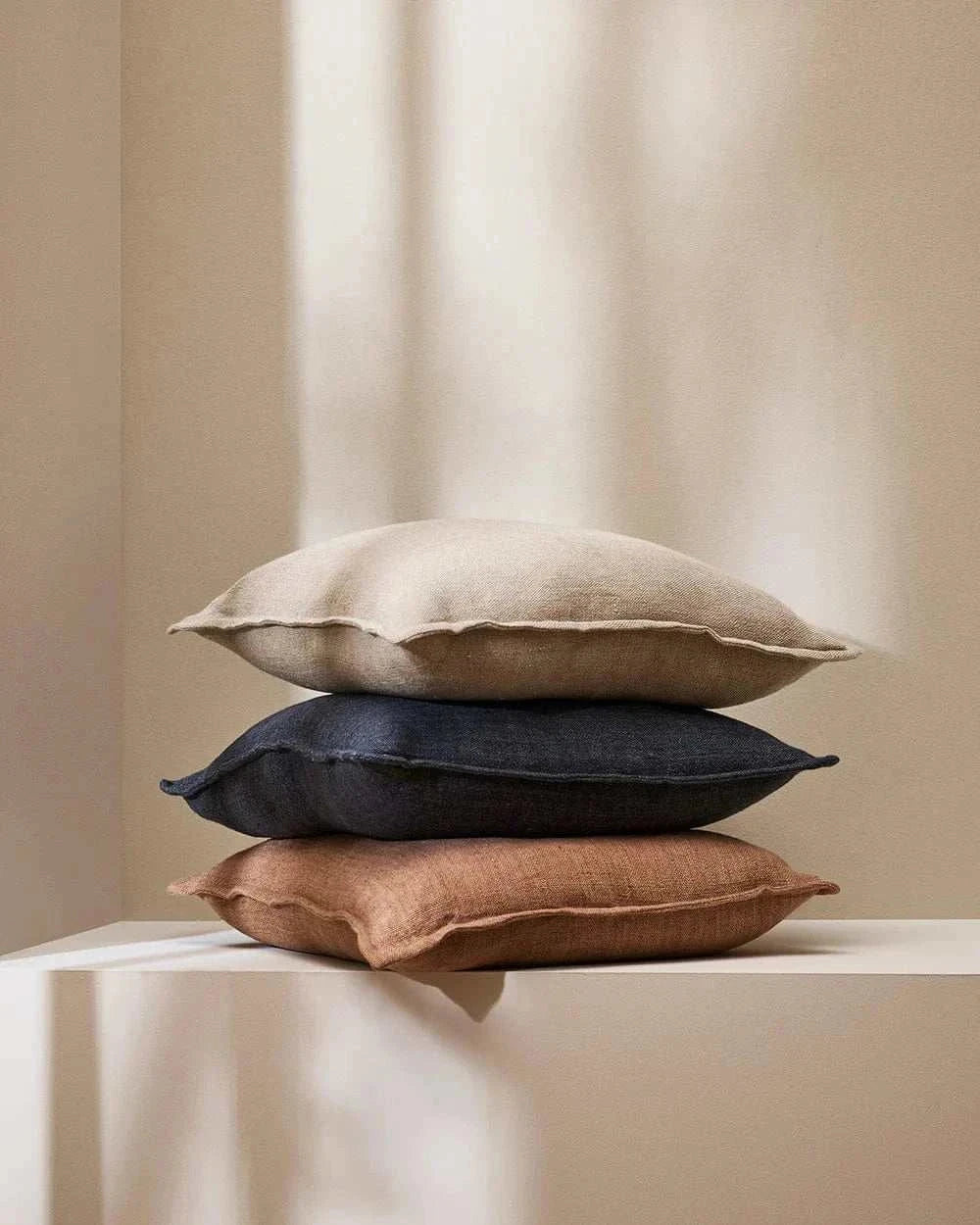 Stack of three Eadie Flaxmill Cushions in neutral, dark blue, and clay colors with linen texture.
