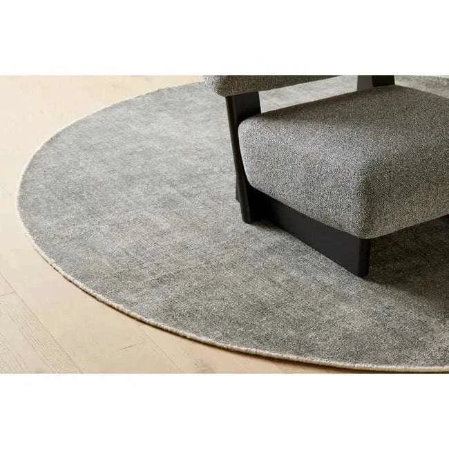 Round dove grey hand-woven GlobeWest Tepih Neptune rug under chair on wooden floor