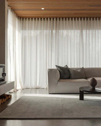 Baya Haywood Floor Rug in slate grey wool placed in modern living room with neutral sofa and sheer curtains