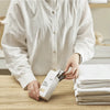 Person holding a box of Thread Design Bed Sheet Bands with folded white bed sheets stacked on a wooden table