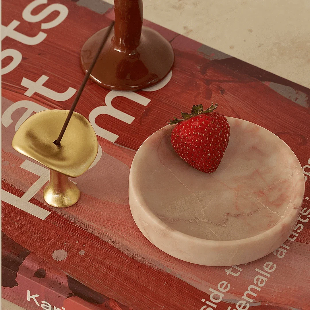 Black Blaze Linea Small Marble Dish in Rosa with smooth edges holding a strawberry on a red surface with a gold incense holder and candle base nearby