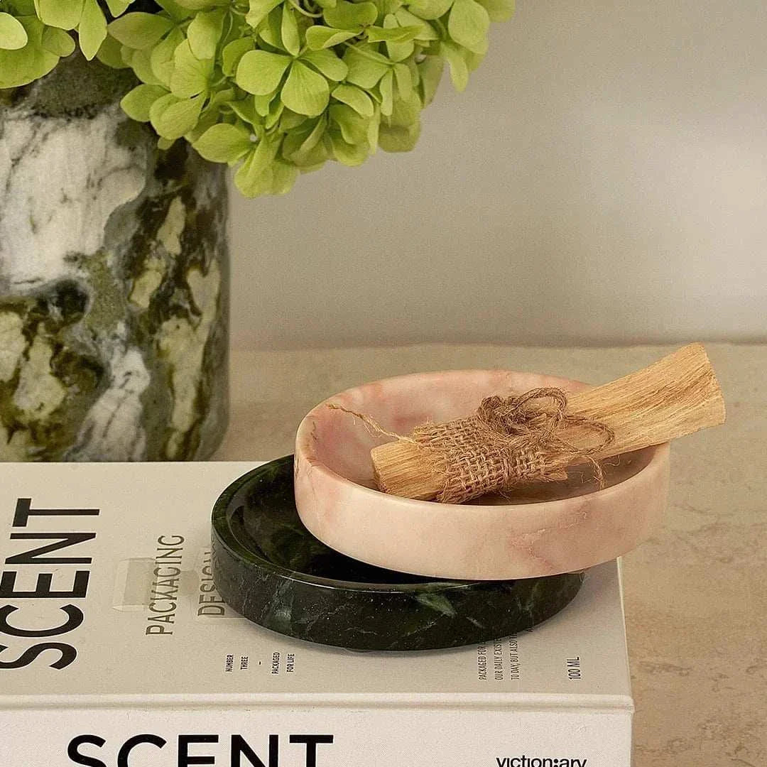 Black Blaze Linea small pink marble dish holding wooden sticks, stacked on a black marble dish on a table with a plant and a book nearby