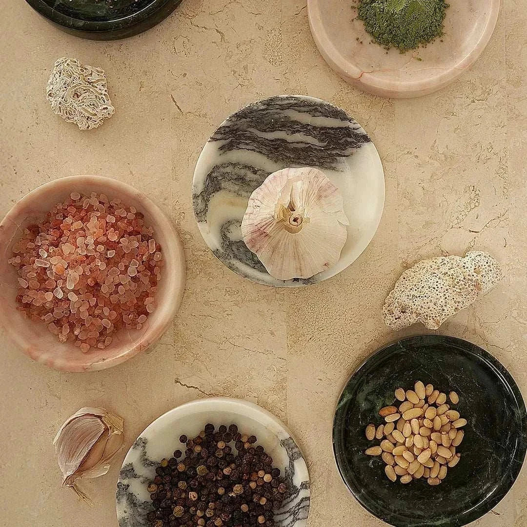 Black Blaze Linea small marble dish in rosa with smooth edges, used for serving spices and displayed with herbs and seeds.