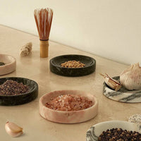 Black Blaze Linea Small Marble Dish in rosa with pink salt on a countertop, surrounded by other marble dishes holding spices and garlic cloves