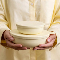 Person holding two light yellow Styleware Nesting Bowls with lids, showcasing different sizes stacked together